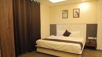 Habitación de hotel con cama, cortinas, mesita de noche, teléfono y dos cuadros colgados en la pared.