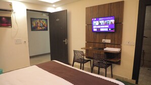 A hotel room with a bed, a desk with two chairs, a TV mounted on the wall, and a door leading to another room. - The Royal Casa Hotel And Banquet (Ghaziabad)