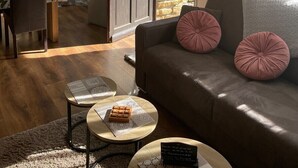 Un salon chaleureux avec un canapé, deux tables basses et un coin repas, la cuisine étant visible au fond.