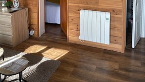 Une pièce aux murs lambrés, avec un lit, un radiateur, une télévision et un bureau doté d’une lampe et d’une radio.