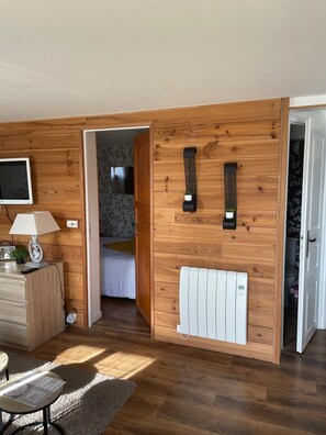 A room with wooden panel walls, a bed, a radiator, a TV, and a desk with a lamp and radio. - Studio-Mountain view-Private Bathroom (Aleu)
