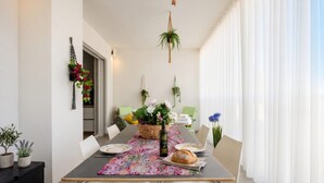 Un coin repas avec une longue table, des chaises, un panier de fleurs, une bouteille et une miche de pain.