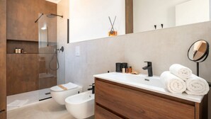 Une salle de bain moderne avec une douche à parois de verre, un bidet, un meuble-lavabo avec un miroir et des serviettes soigneusement pliées.