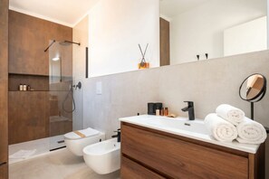 Ein modernes Badezimmer mit Duschkabine aus Glas, einem Bidet, einem Waschtisch mit Spiegel und ordentlich aufgerollten Handtüchern.
