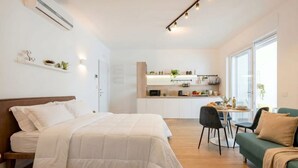 Une chambre avec un lit, un canapé vert, un coin repas avec une table et des chaises, et une petite cuisine en arrière-plan.