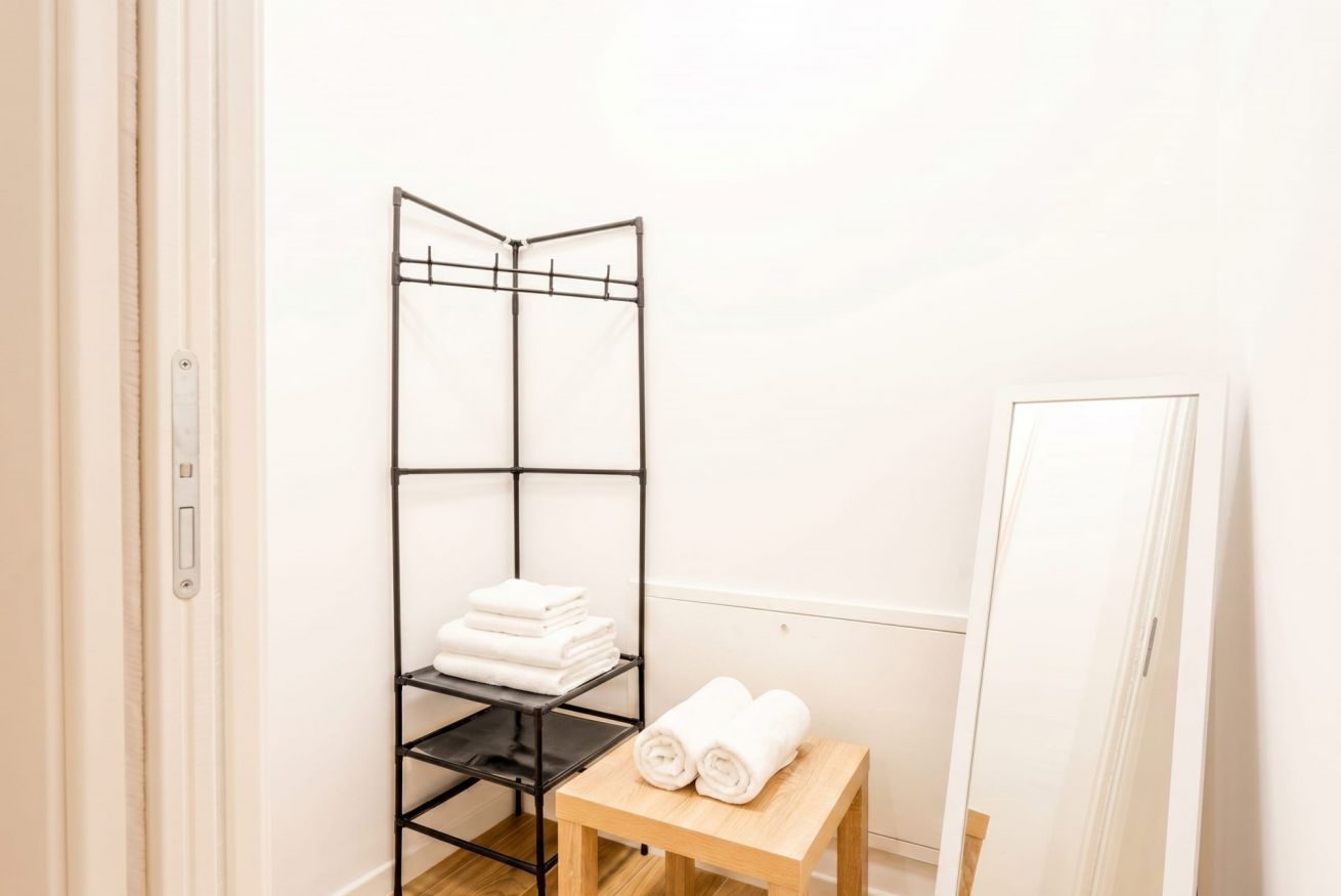 Una habitación con una estantería metálica negra que contiene toallas dobladas, una mesa de madera con toallas enrolladas y una puerta blanca.