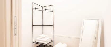 A room with a black metal shelf holding folded towels, a wooden table with rolled towels, and a white door.