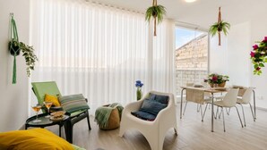 Un salon moderne avec un coin repas, de grandes fenêtres ornées de rideaux légers et des plantes suspendues.