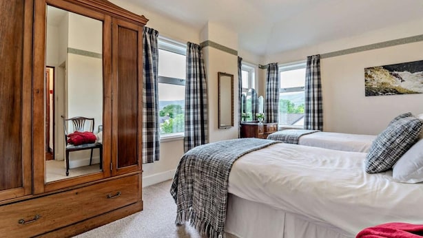 A bedroom with a large wooden wardrobe, two beds, a chair, a mirror, and a painting on the wall. - Dunoon - Sleeps 17 - Group Retreat With Parking (Dunoon)