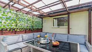 A covered patio with a glass table, wicker furniture, and a green leafy wall. - Dunoon - Sleeps 17 - Group Retreat With Parking (Dunoon)