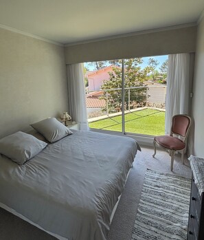 A bedroom with a bed, a chair, a nightstand, and a view of the outside.