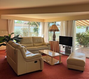 Un salon comprenant un canapé, un pouf, une table basse, un téléviseur et une lampe.