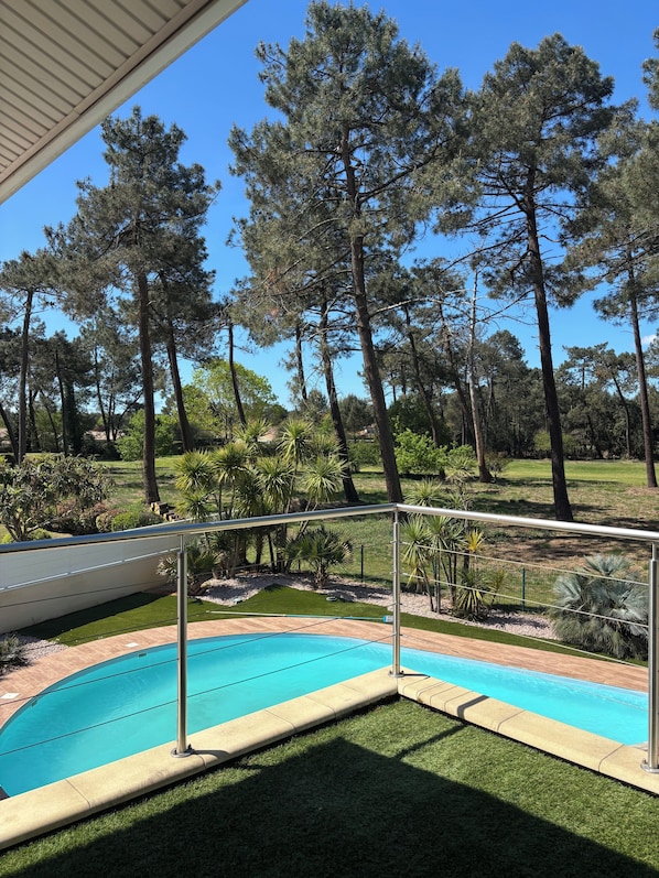 A swimming pool with a metal railing, surrounded by a well-maintained lawn and tall pine trees.