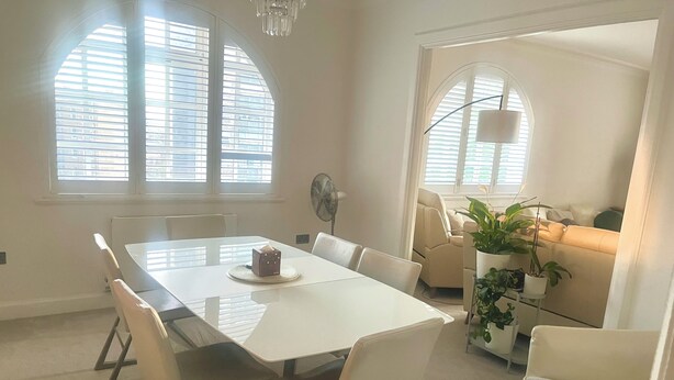 A dining area with a table, chairs, and a fan. There are windows with blinds, a sofa, and a potted plant. - Fabulous 2-bedroom apartment in NW8 London perfect for your stay (London)