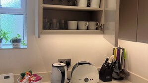 A kitchen with a coffee maker, toaster, and utensils on the counter, and a cabinet above with various kitchenware. - Fabulous 2-bedroom apartment in NW8 London perfect for your stay (London)