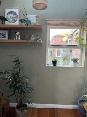 Ein Zimmer mit einem großen Fenster, einem hölzernen Regal mit Dekoration und einem Blumentopf.