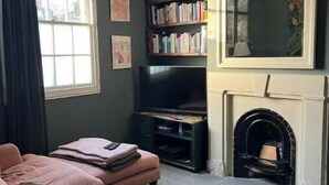 A living room with a sofa, a television, bookshelves, a fireplace, and a chandelier. - Stylish Family Home with Garden near Tottenham Stadium & Easy Central Access (London)