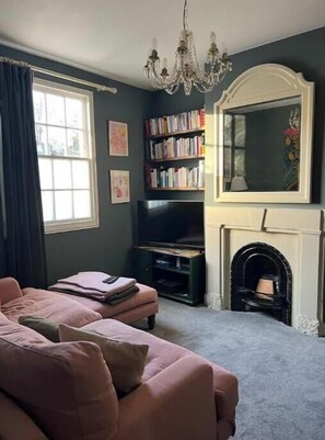 Ein Wohnzimmer mit einer Couch, einem Fernseher, Bücherregalen, einem Kamin und einer Kristallleuchter.