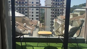 Un balcón con vistas a edificios circundantes, una pequeña mesa y dos sillas de mimbre.