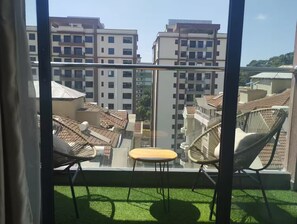 Ein Balkon mit Blick auf umliegende Gebäude, einem kleinen Tisch und zwei Korbstühle.