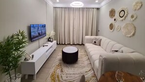 Una sala de estar moderna con un televisor de pantalla plana, un sofá blanco, una mesa de centro y detalles decorativos en la pared.