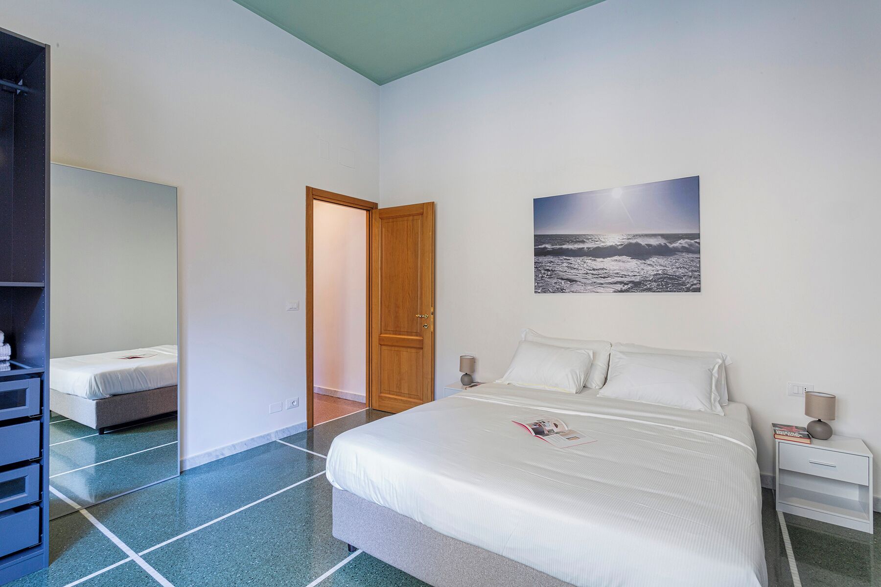 Une chambre à coucher comprenant un lit, une table de chevet, une lampe de chevet, une porte et un tableau accroché au mur.
