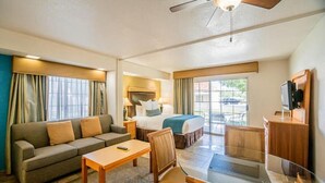 Hotelkamer met een bed, bank, eettafel, stoelen, televisie en plafondventilator.