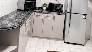 Eine moderne Küche mit weißen Schränken, einer schwarzen Arbeitsplatte, einer Mikrowelle, einem Toaster, einem Kühlschrank und einem kleinen Topfpflanzen.