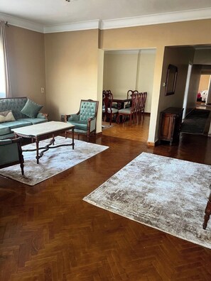 A spacious living room with a sofa, a chair, a dining table with chairs, and a staircase leading to another level. - Spacious Apartment Cairo (Cairo Governorate)