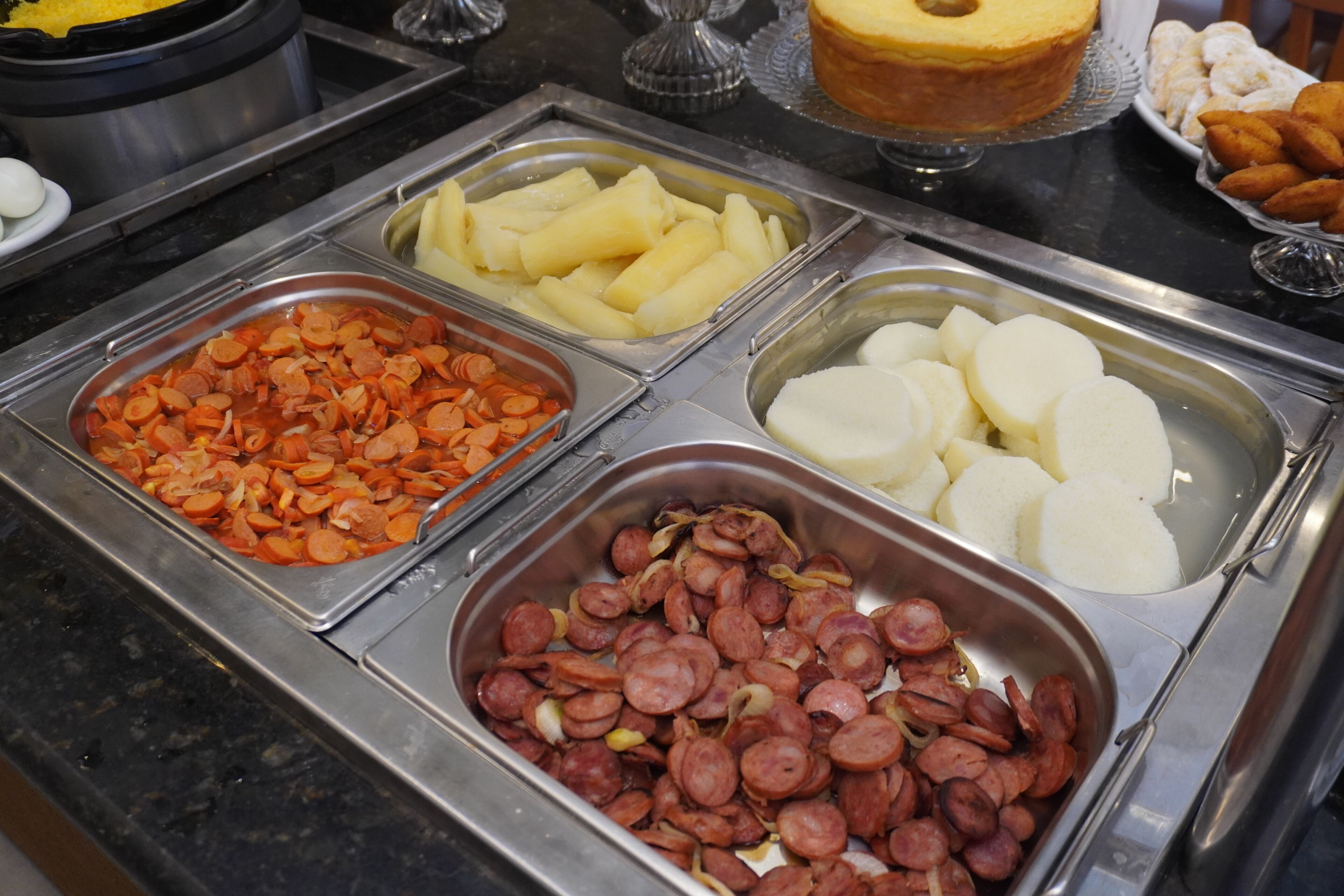 Un buffet proposant une variété d’aliments, notamment des saucisses en tranches, des carottes, des pommes de terre et des aliments ronds de couleur claire.