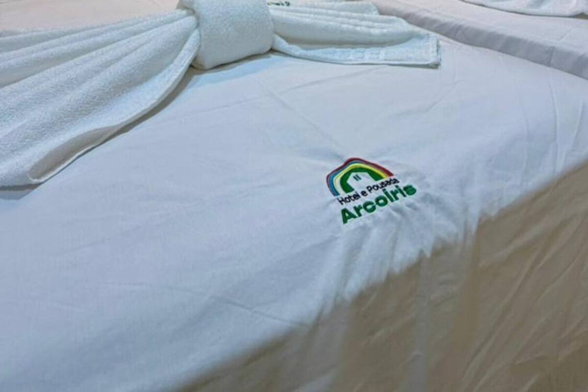 A hotel room with two beds, white bedding, a headboard, a towel, and a logo on the bedspread.