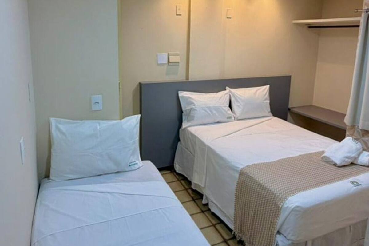 A hotel room with two single beds, a small bathroom, and a tiled floor.
