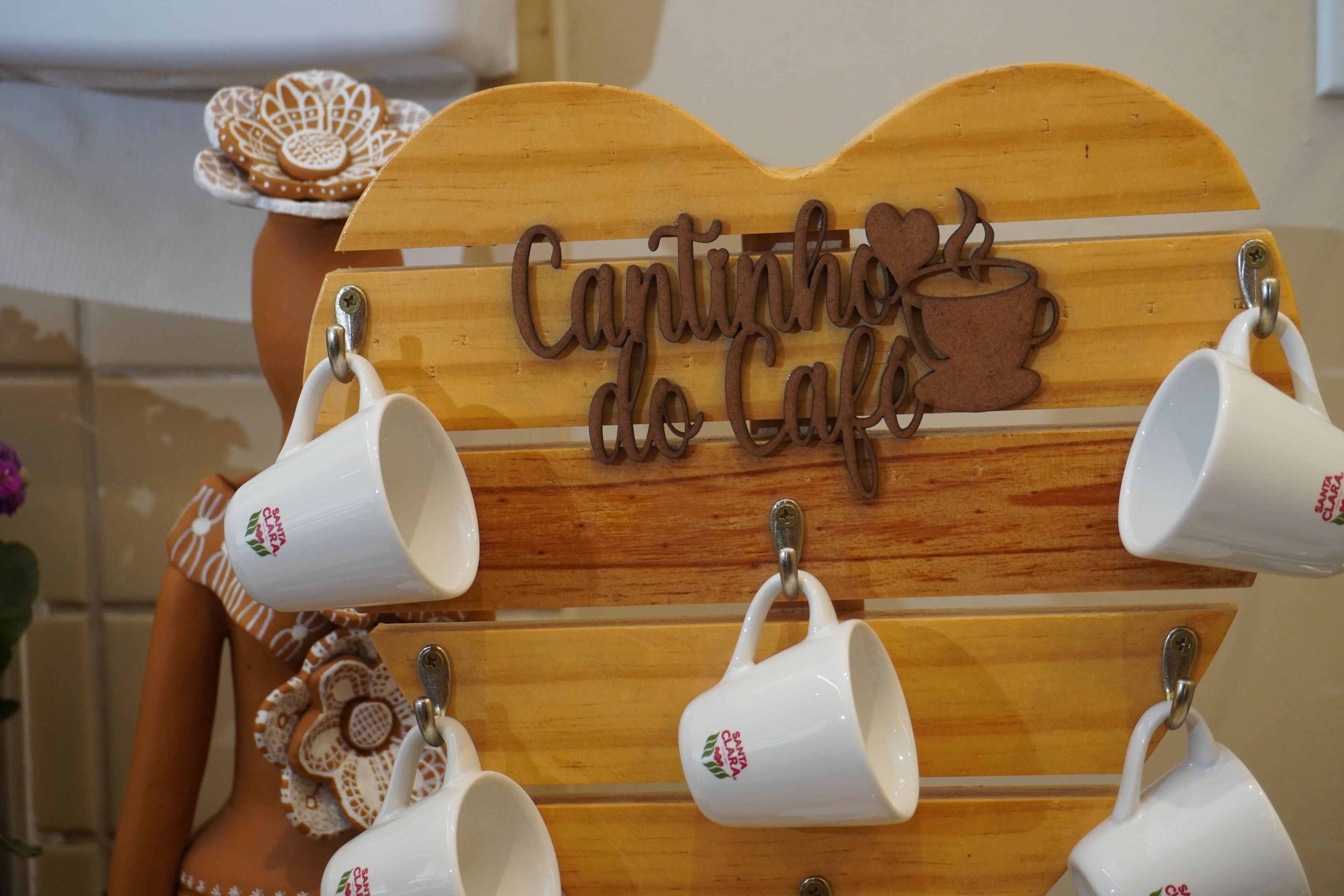 Un letrero de madera con tazas colgando y una pieza decorativa de cerámica con motivos florales.