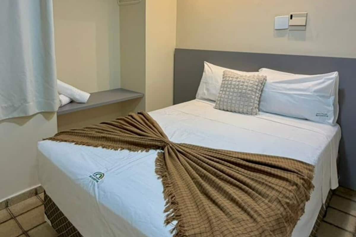 Quarto de hotel com cama, guarda-roupa, banheiro e luminária no teto.