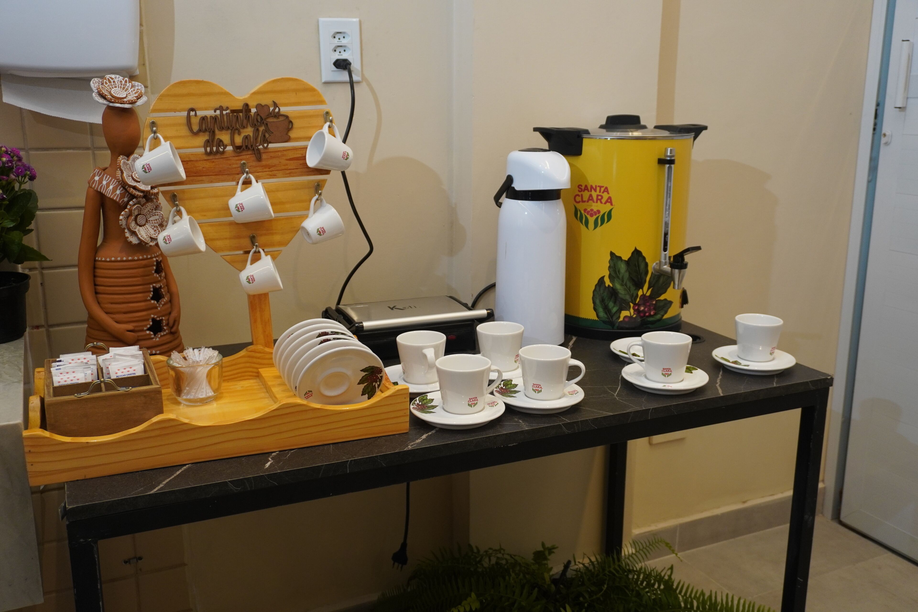 A coffee station with a decorative mannequin, white cups, saucers, a coffee maker, and a tray with sugar packets.