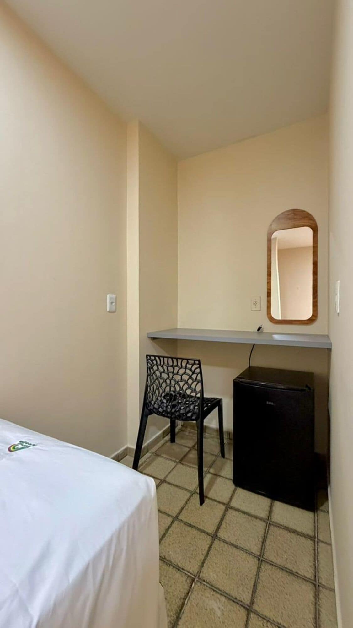 Una habitación pequeña y poco amoblada, con una cama, un escritorio, una silla y un espejo.