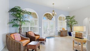 A spacious living room with wicker furniture, a chandelier, and large windows with shutters. - Mar3507 3 Bedroom Home (Punta Gorda)