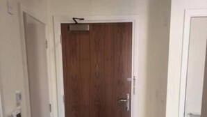 Um corredor com porta de madeira, tapete estampado e parede branca.