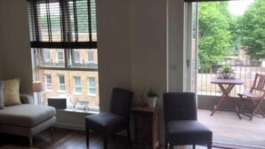 Uma sala de estar com um sofá, duas cadeiras, uma mesa pequena com uma planta e um painel de vidro deslizante que dá para um pátio externo.
