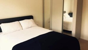 Cama com roupa de cama branca, cabeceira preta e manta preta.