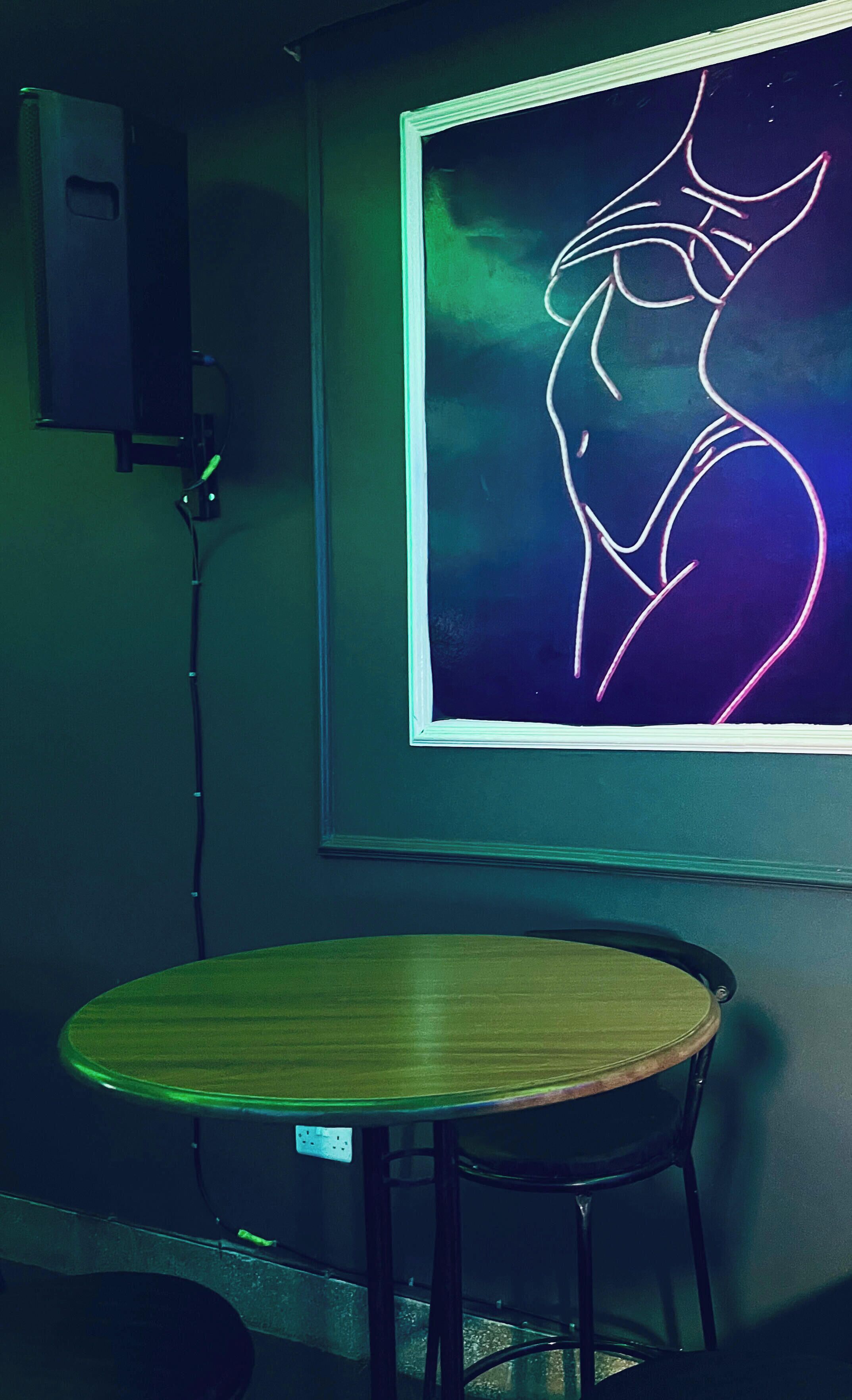Una habitación con una mesa redonda y una silla, una obra de arte abstracto colgada en la pared y un enchufe.