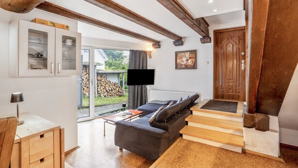 Una sala de estar moderna con un sofá, televisor, escalera de madera y vistas al exterior.