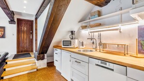 Una cocina con encimera de madera, armarios blancos, microondas, cafetera y un lavabo.