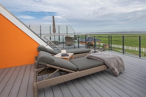 Ein Balkon mit Korbmöbeln, Blick auf eine grüne Landschaft und ein Gebäude mit einem geneigten Dach.