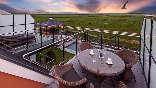 Una terraza en la azotea con mobiliario exterior, piscina y vistas a una granja con animales.