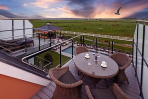 Una terraza en la azotea con mobiliario exterior, piscina y vistas a una granja con animales.