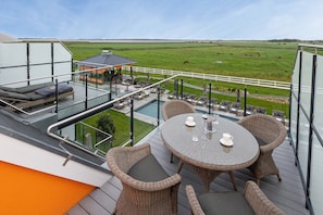 Terraza en la azotea con mobiliario exterior, piscina y vistas a un campo verde.