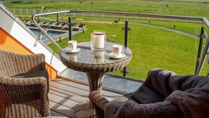Un balcón con mobiliario de mimbre, una mesa de vidrio con velas y vistas a un campo verde.
