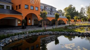 Un edificio moderno con una fachada naranja distintiva, múltiples entradas y una fuente reflectante en primer plano.
