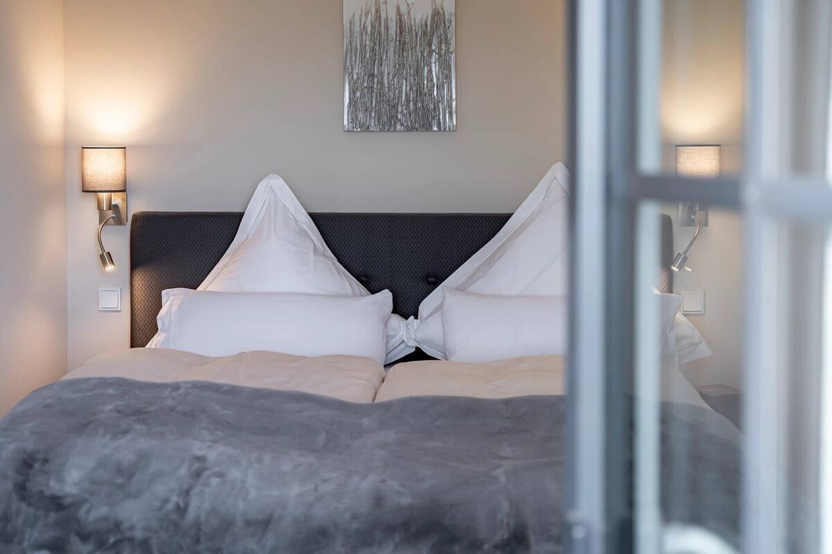 A modern hotel room with a bed, two wall-mounted lamps, and a textured wall art piece.